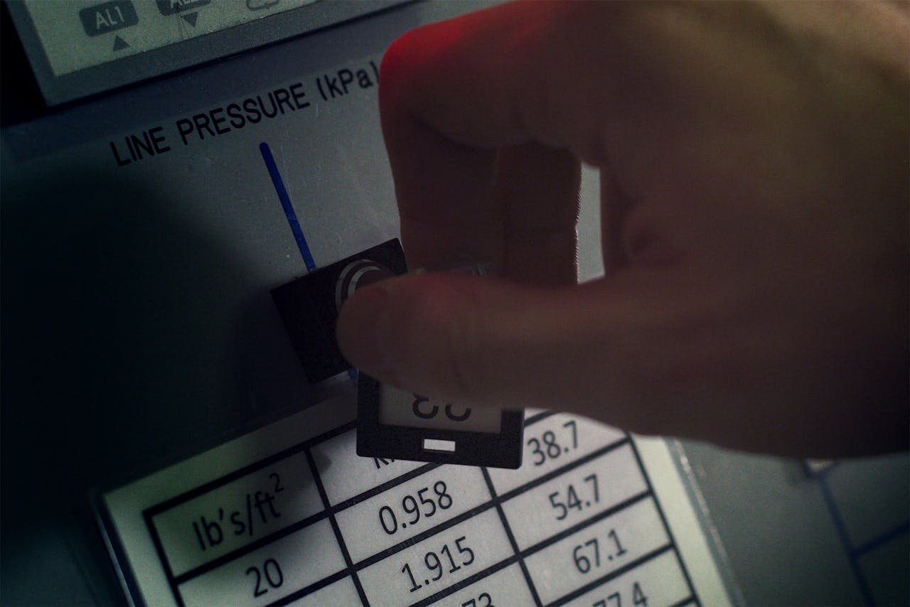 Close-up of hand adjusting pressure gauge dial in an industrial setting with visible pressure readings and controls.